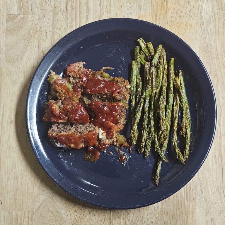 Sliced full-blood Wagyu meatloaf with tomato glaze served with roasted asparagus on a navy blue plate