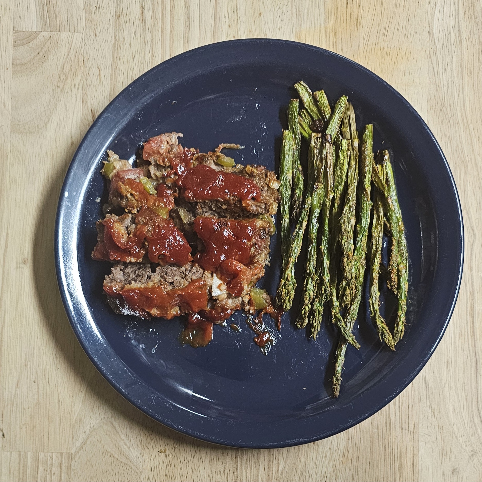 Sliced full-blood Wagyu meatloaf with tomato glaze served with roasted asparagus on a navy blue plate